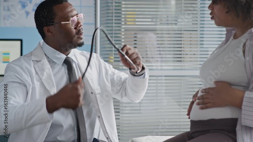 Medium hot of Black male healthcare professional examining pregnant woman using stethoscope in clinical setting, ensuring prenatal care and fetal health monitoring
