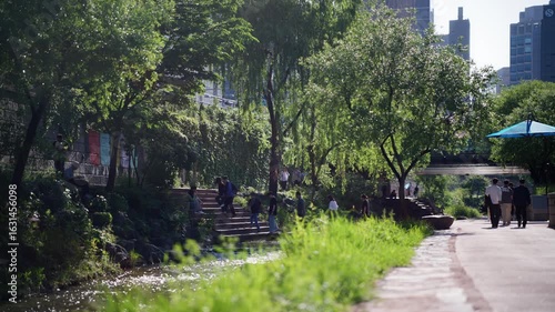 People Walking Along a Scenic Urban Stream Surrounded by Lush Greenery — South Korea, Seoul, Cheonggyecheon, downtown, city