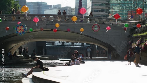Colorful Lanterns and People Enjoying a Sunny Day by the Water Under a Bridge — South Korea, Seoul, Cheonggyecheon, downtown, city