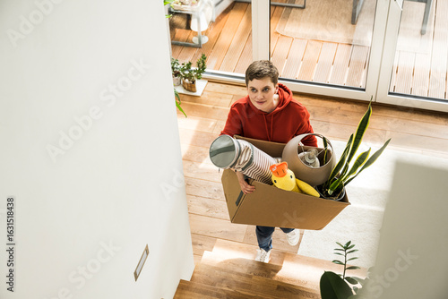 Woman carrying box while moving and cleaning up at home happily