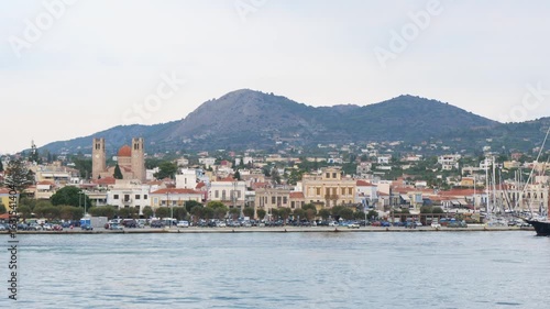 Wallpaper Mural Evening view of a picturesque coastal town on Aegina island, Greece, with calm harbor waters, docked boats, a church with twin bell towers, Mediterranean houses, and lush mountains in the background Torontodigital.ca