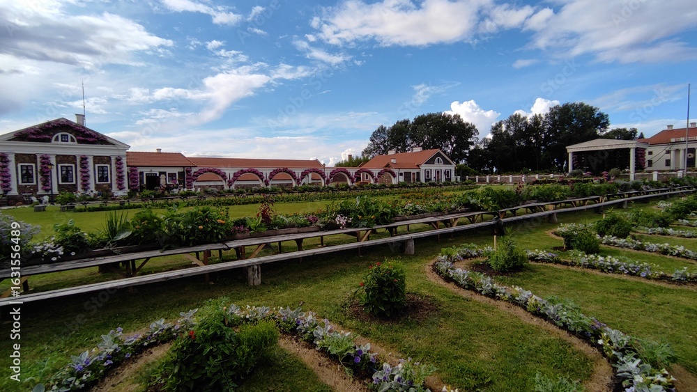 Naklejka premium Well-maintained manor park surrounded by blooming flower beds. An elegant and romantic setting perfect for photoshoots or nature walks