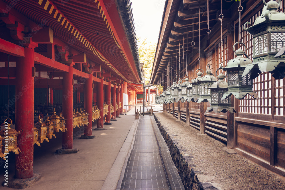 Fototapeta premium Symmetrical rows of golden and bronze lanterns hanging in eastern corridor of Kasuga Taisha Shrine Nara Japan with traditional architecture and warm vintage lighting