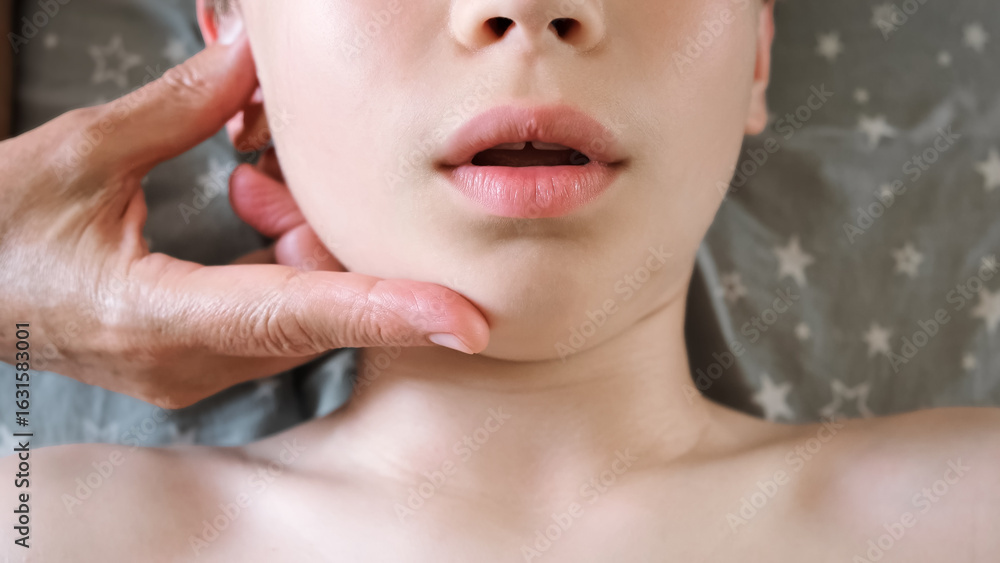 Naklejka premium The masseur is massaging child's face. A session of therapeutic lymphatic drainage massage. Physiotherapy treatment. An osteopath removes tension from the jaw muscle and relieves pain in a joint.