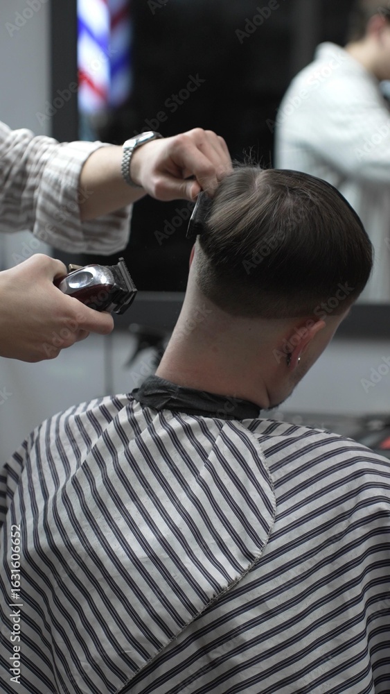 Fototapeta premium Professional barber carefully trimming customer's hair with electric clipper, providing a stylish and precise haircut in a modern barbershop environment