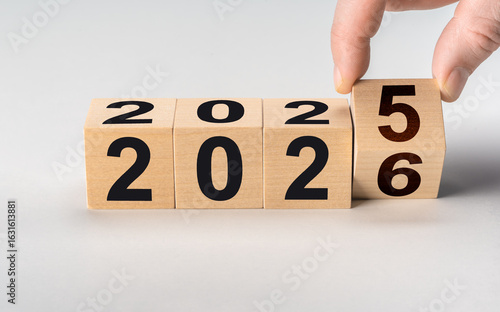 Fingers flipping wooden block to change date from 2025 to 2026. New year's eve and fresh start business concept