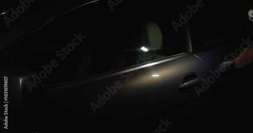 A car thief in black gloves pulls the car door handle at night, trying to rob or steal a car.Concept for advertising the installation of alarm systems or guarded parking