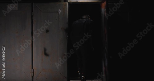Kyiv, Ukraine 24.08.2023  View of the garage at night through the opened door. A guy in motorcycle gear puts on a helmet, gets on a motorcycle and  ready to ride, turning on the headlight