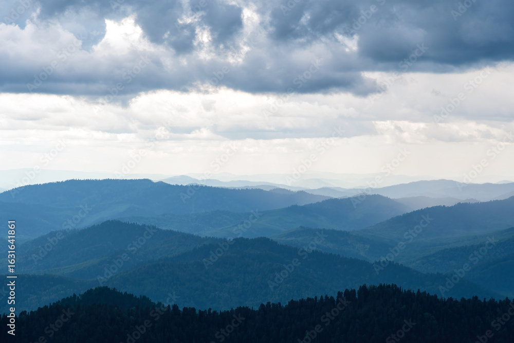 Fototapeta premium Layers of blue mountains recede into the distance under a cloudy sky, creating a sense of depth and serenity
