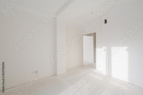 stark, white room under construction.  Bright light streams through unseen windows. An open doorway leads to another space