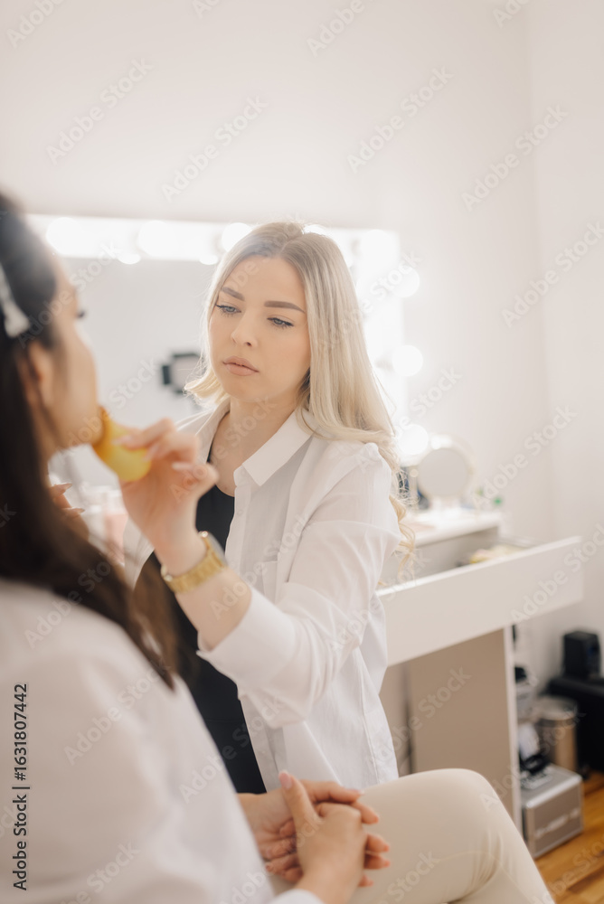Fototapeta premium Professional makeup artist applying foundation on model's face in beauty salon
