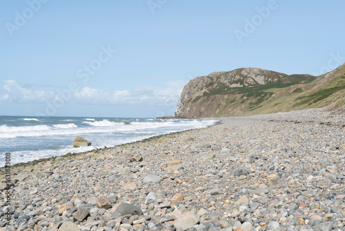 Deserted pebble beach at Pistyll, Lleyn Peninsular, Wales, UK, with views to a headland against a blue sky with clouds.