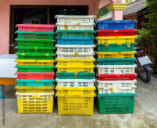 A medium shot captures three vertical stacks of colorful, weathered plastic crates. The crates are arranged in a repeating pattern of white, red, yellow, and green, suggesting their use for a market