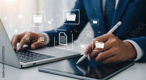 Business professional using laptop and digital tablet with file management icons. Futuristic digital workspace concept. Tech-savvy professional organizing data.