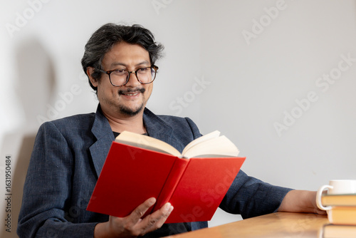 Relaxed young man wearing glasses enjoying reading a book in a cozy home environment.