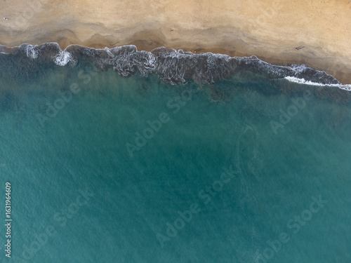 Wonderful tropical beach with blue water and orange sand forming small waves seen from above