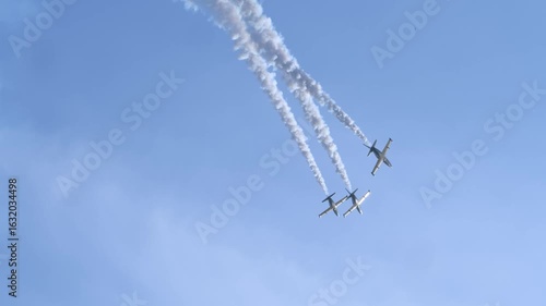 A group of airplanes, illuminated by the bright sun, fly away into the distance, leaving behind trails of condensed white smoke.