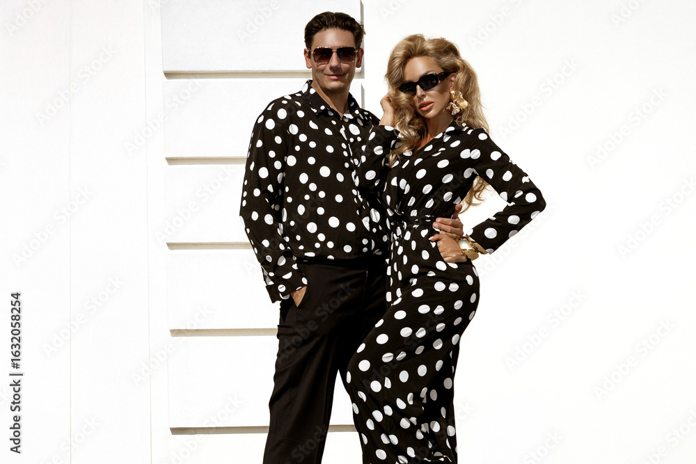 Fototapeta premium Fashionable Female Model and Male Model in Matching Black and White Polka Dot Elegant Outfits Posing Outdoors in Summer Sunny Day. Polka Dot Fashion. Retro