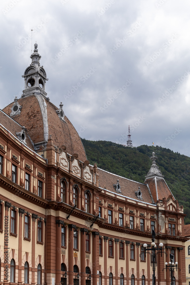 Obraz premium view of the brasov city hall building with its distinctive architecture and dome, set against the backdrop of tampa mountain. the scene captures a blend of urban life and nature