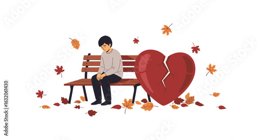 Sad young man sits alone on park bench beside broken heart with falling autumn leaves