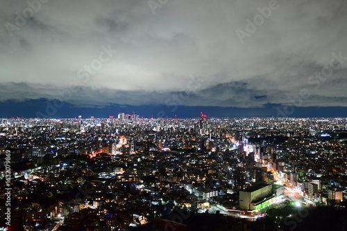 City at night, glowing buildings beneath dramatic cloudy sky.