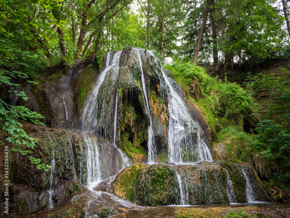 Fototapeta premium Lúčky Waterfall, travertine cascade in TANAP, Slovakia. Natural monument with clear water falling into mossy rocks, surrounded by forest vegetation.