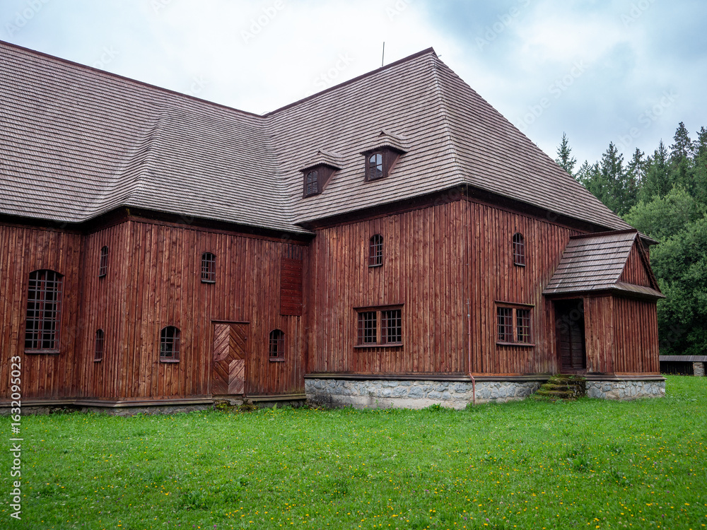 Obraz premium Side view of the wooden articular church in Svätý Kríž, Slovakia. Historic Lutheran church built from timber without nails, surrounded by green grass and trees.