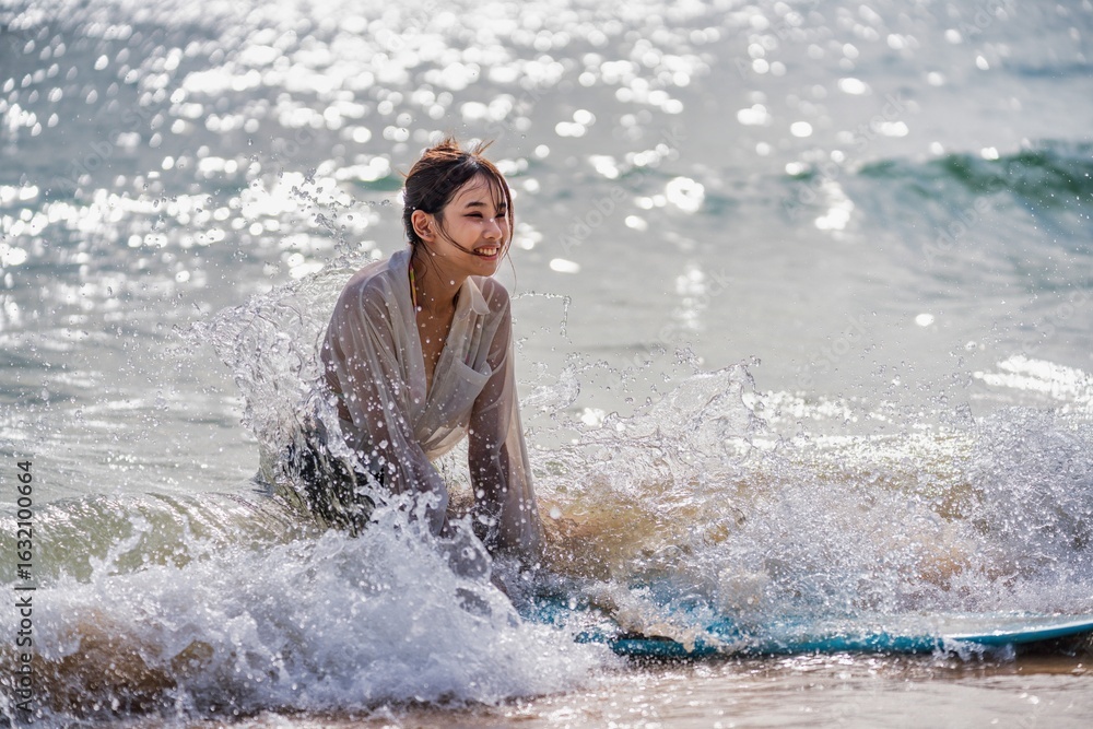 Fototapeta premium Young woman enjoys surfing on a sunny beach while playing with ocean waves during the day