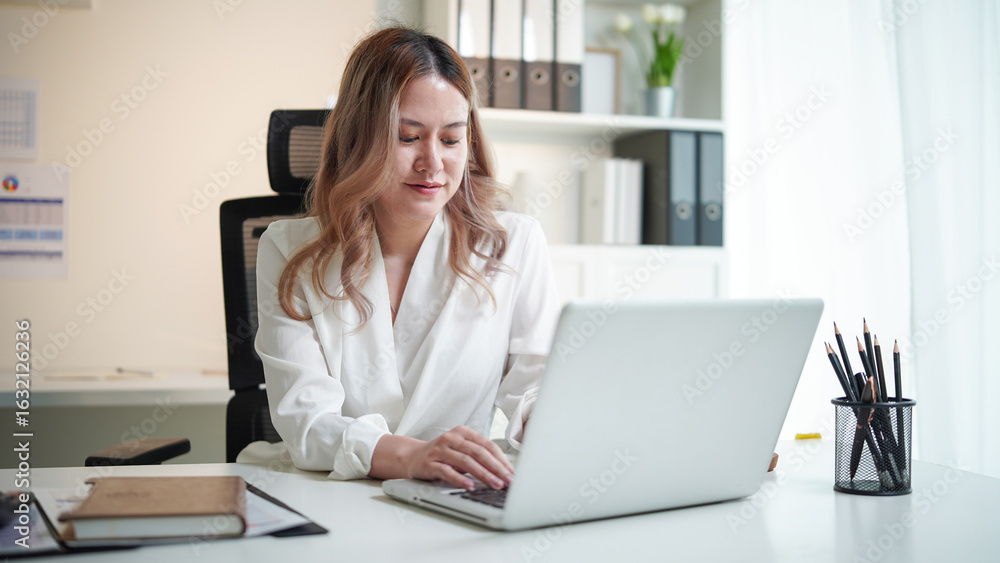 Confident young businesswoman using a laptop in a bright office space. Confident young businesswoman using a laptop in a bright office space.
