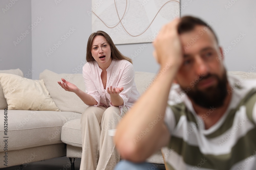 Fototapeta premium Betrayal. Angry woman shouting at her offended husband on sofa at home, selective focus