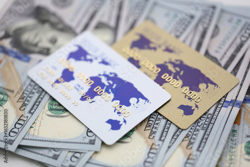 Colorful credit cards resting on a stack of hundred-dollar bills during a sunny afternoon in a bustling city market