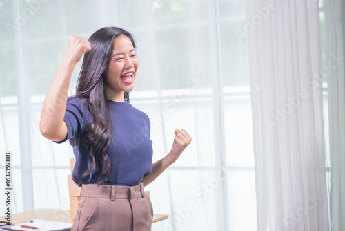 Free Download A young Asian entrepreneur smiles as she types on her laptop, managing inventory, packing packages and checking orders for her online startup business. - GFXLoad