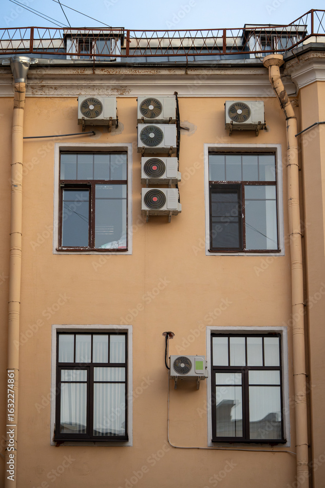 Obraz premium Facade of building with many air conditioners on windows in southern hot country. Yellow house exterior on city street. Escape from heat, creating favorable microclimate in urban apartments concept.