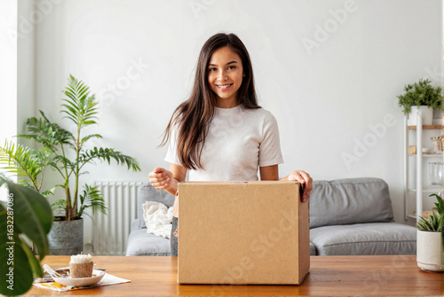 Une jeune femme souriante ouvre un colis écologique chez elle