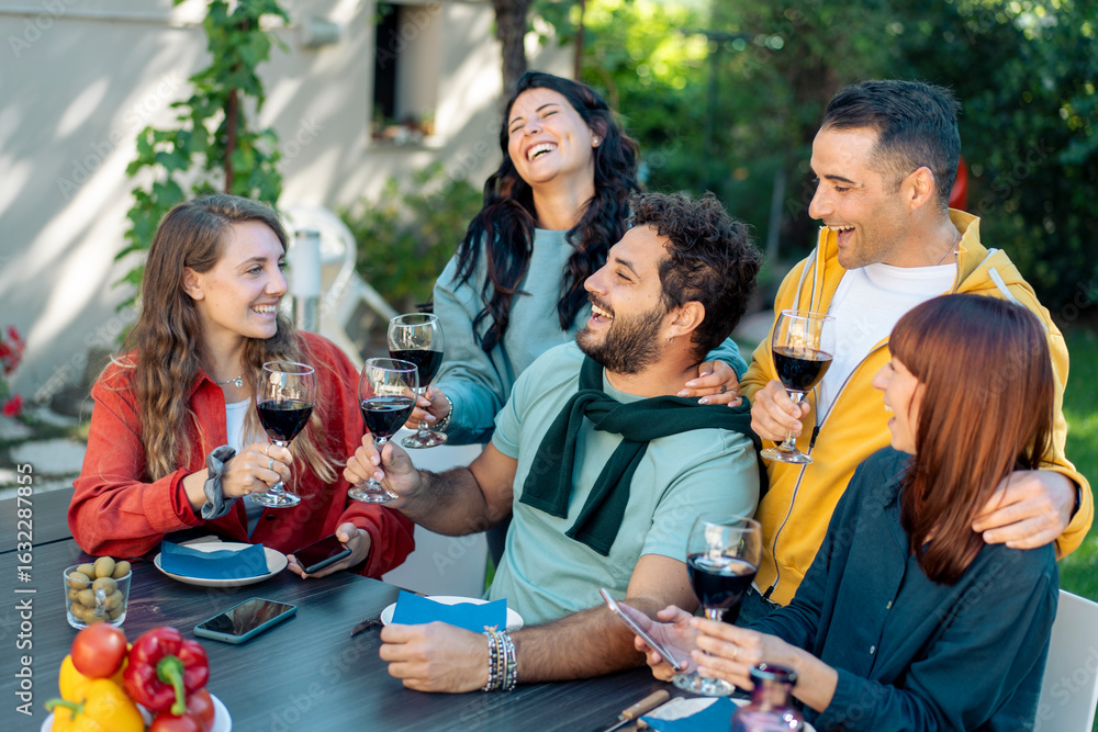 Obraz premium Group of young friends socializing and drinking red wine on a terrace during a summer aperitivo.