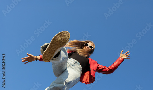 Dynamic low angle shot of a young woman boldly stepping forward against a clear blue sky. vitality, freedom and joy, motivation to move. copy space.