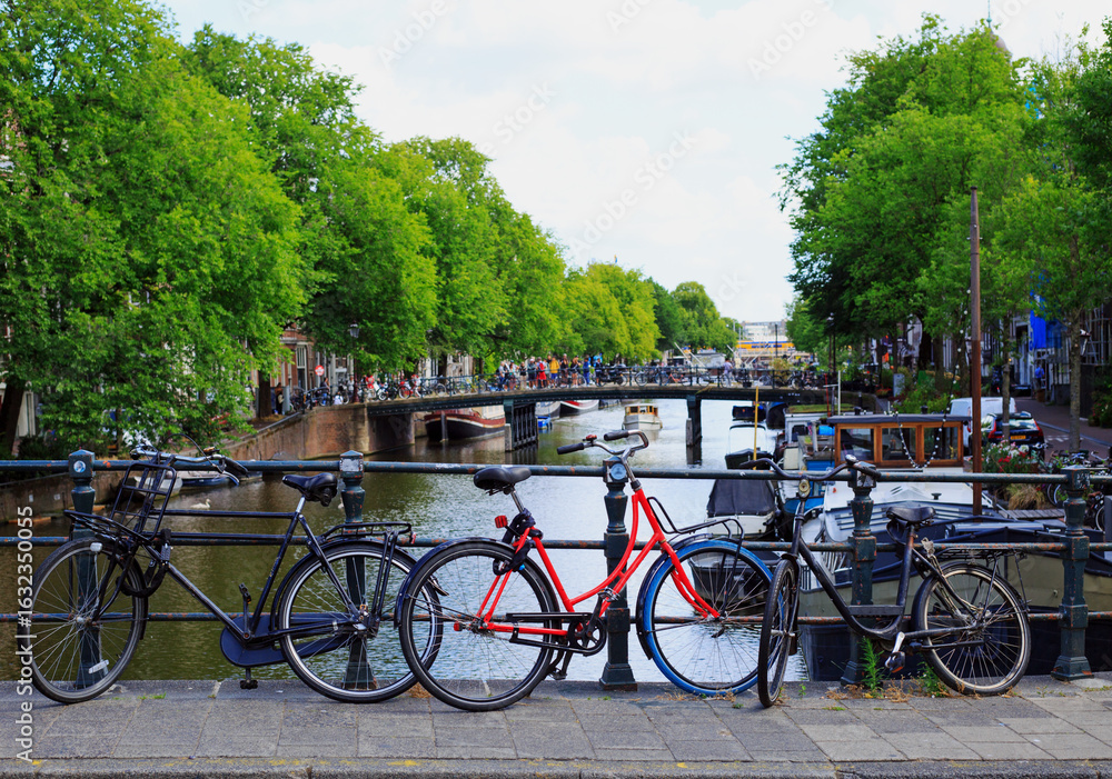 Fototapeta premium Amsterdam with bicycles leaning against a railing with a canal view in the background