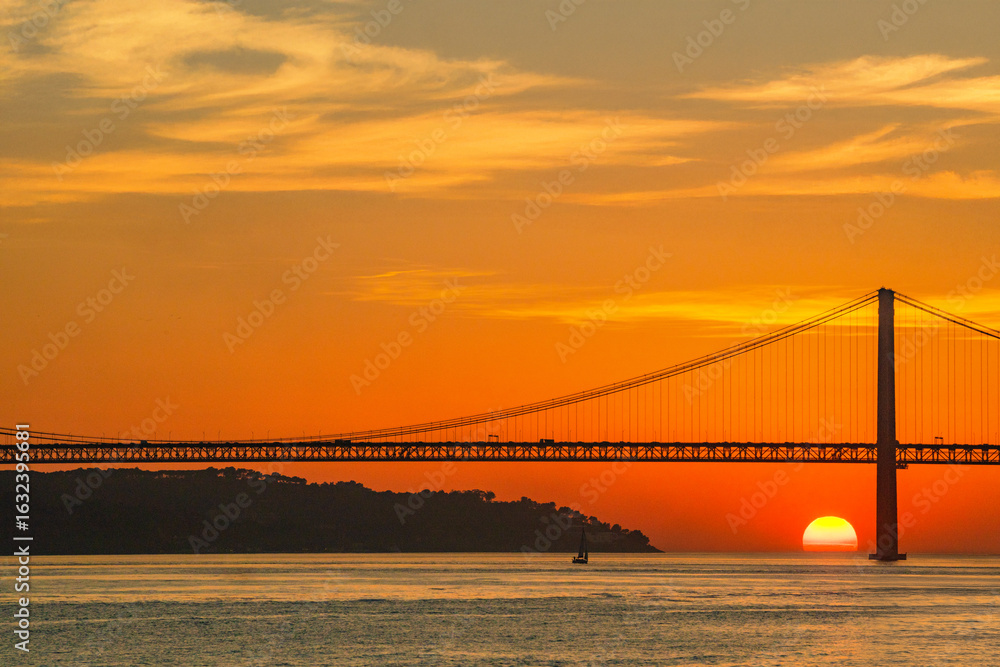 Obraz premium Golden hour over the Tagus River with Lisbon iconic 25 de Abril Bridge. Ideal for souvenirs postcards magnets editorial design blogs and travel websites.