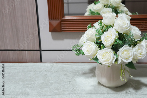 Elegant bouquet of white roses in a vase sitting on a table in front of a mirror.