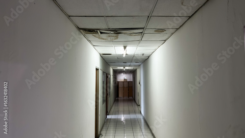 Long Empty Hallway with Damaged Ceiling and Fluorescent Lights in an Old Building.