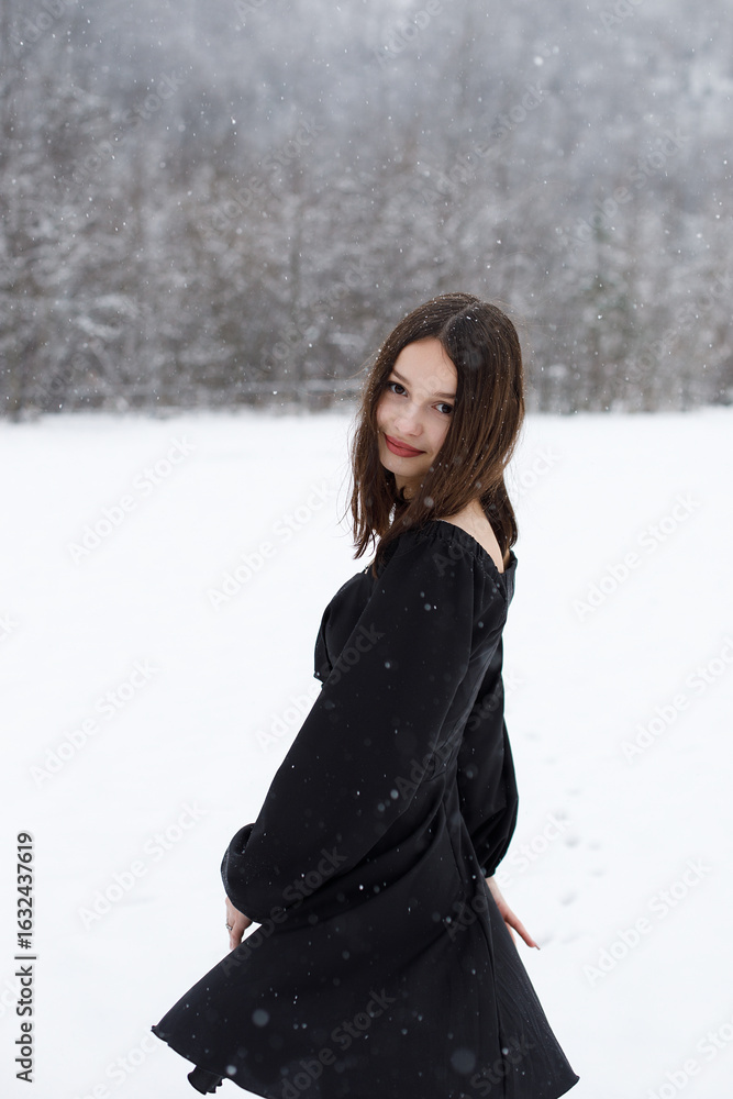 A girl stands in a field in a short dress against the backdrop of mountains and heavy snowfall. A girl stands in a field in a short dress against the backdrop of mountains and heavy snowfall.