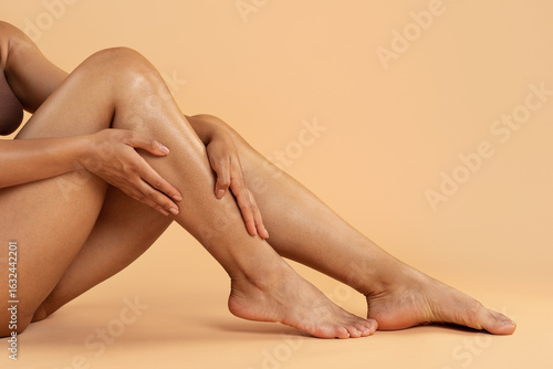 Foto Seated black woman caressing her legs in relaxed pose on beige background