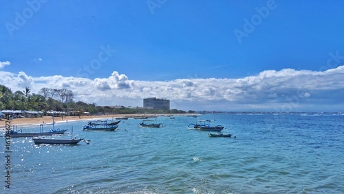 Landscape of beach in Bali, Indonesia. Traditional boats(Jukung boat)dotting the turquoise water under a vibrant blue sky with fluffy clouds