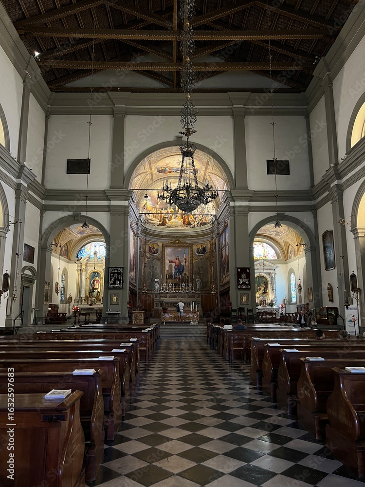 Fototapeta premium Palmanova, Italy - July 15, 2025: Interior view of historic church featuring wooden pews, ornate altar, and beautiful stained glass windows with copy space