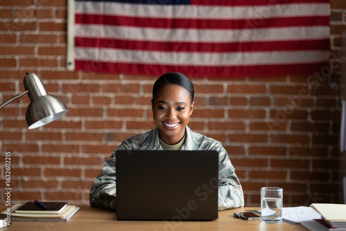 Smiling Military Woman Working on Laptop at Desk with American Flag Background