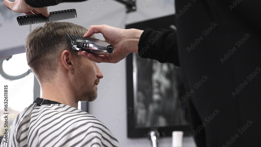 Fototapeta premium Professional barber trimming male client's hair using electric razor, creating precise haircut in contemporary barbershop setting with sleek styling tools