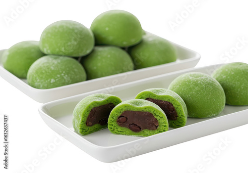 A display of green mochi on white trays, some cut open to reveal the red bean paste filling inside them on transparent background