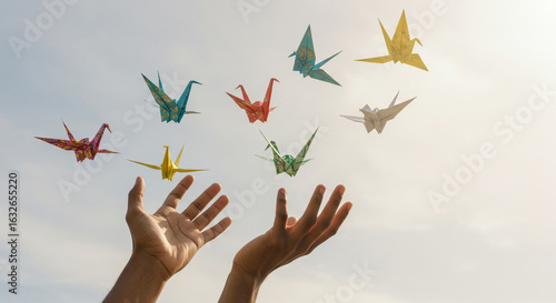 Hands releasing colorful origami cranes into the bright sky  