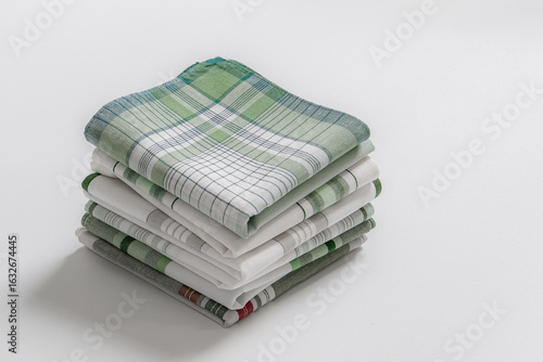 Stack of clean, folded men's handkerchiefs with green stripes and plaid designs on a white background.