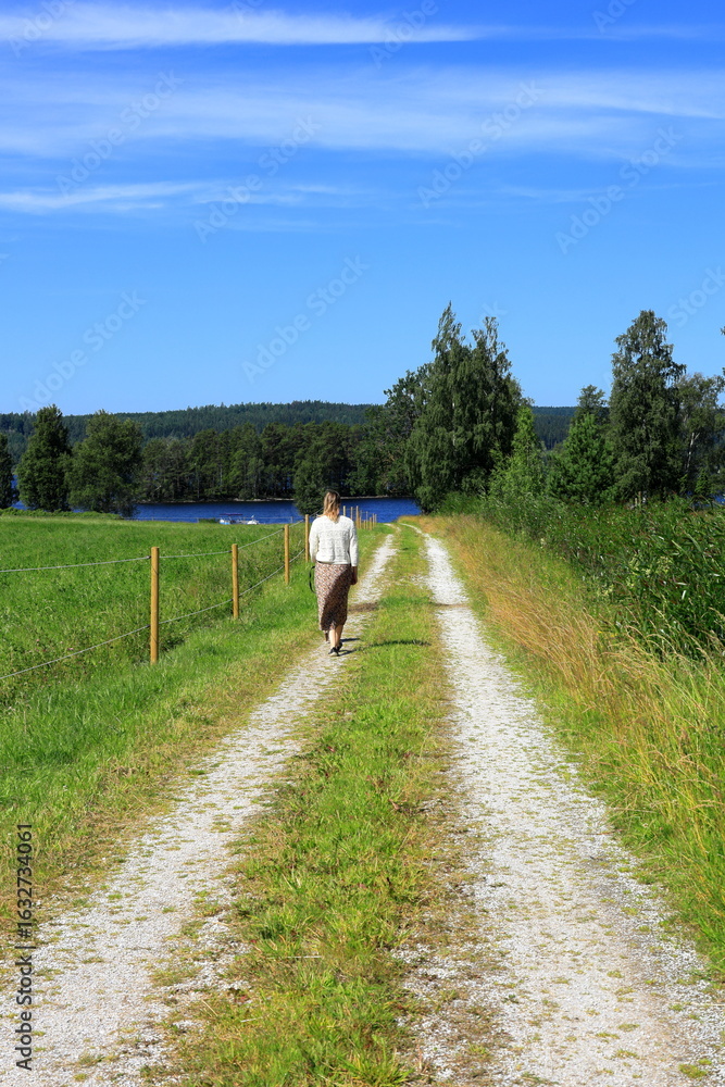 Obraz premium Woman walking at country road one summer day. Bergslagen, Sweden.